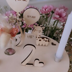 Pu&ograve; includere: Topper per torta di compleanno in legno con una giraffa, un palloncino con la scritta "Melina", un vaso con fiori e il numero "2". La base del topper dice "Heute ist dein Tag" e "02.11.2021".