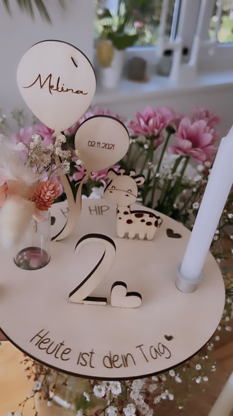 Pu&ograve; includere: Topper per torta di compleanno in legno con una giraffa, un palloncino con la scritta "Melina", un vaso con fiori e il numero "2". La base del topper dice "Heute ist dein Tag" e "02.11.2021".