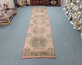 May include: A vintage pink and cream runner rug with a geometric pattern. The rug has a faded look and is made of wool.