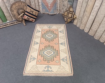 May include: A light pink and cream colored rug with a geometric pattern in shades of green and blue. The rug has a fringe border.