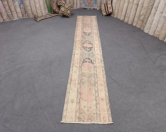 Peut inclure: Un tapis long et étroit avec un fond beige et un motif répétitif de formes géométriques roses, noires et blanches. Le tapis a une frange aux deux extrémités.