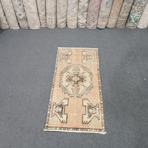 May include: A small, light beige rug with a brown geometric pattern. The rug has a central medallion with four smaller medallions in the corners.