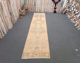 May include: A beige runner rug with a geometric pattern in shades of brown and blue. The rug has a fringed edge and is laid out on a gray floor.
