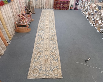 Peut inclure: Un tapis long et étroit avec un fond crème et un motif floral bleu et brun. Le tapis est posé sur un sol gris.