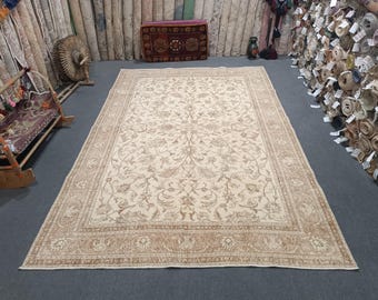 Könnte beinhalten: Ein großer, cremefarbener Teppich mit einem floralen Muster in einem dunkleren Braunton. Der Teppich hat einen Rand mit einem komplizierteren Design.