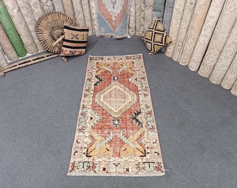 Puede incluir: Una alfombra de estilo vintage con un esquema de color rojo, naranja y crema. La alfombra tiene un patrón geométrico con una forma de diamante central. La alfombra mide aproximadamente 76 cm de ancho y 152 cm de largo.