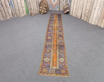 Peut inclure: Un tapis long et étroit avec un motif géométrique coloré. Le tapis a une bande orange centrale avec des motifs floraux bleus et verts de chaque côté.