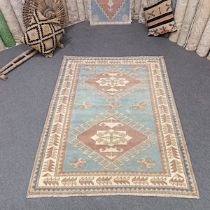 Puede incluir: Una alfombra turca vintage con un patrón geométrico azul, beige y rojo. La alfombra tiene un borde con flecos y está en buen estado.