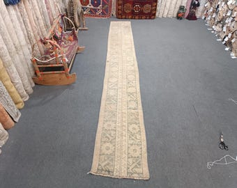 Peut inclure: Un long tapis de couloir blanc cassé avec un motif traditionnel dans une nuance de vert plus claire. Le tapis a une bordure frangée et est posé sur un sol gris.