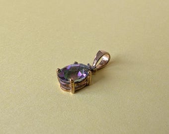 May include: A gold-colored pendant with a large, oval-shaped, iridescent gemstone. The gemstone displays a blend of purple, green, and blue hues. The pendant has a simple, elegant design, suitable for necklaces or other jewelry.