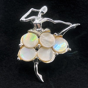 May include: Silver-toned ballerina brooch with a skirt of iridescent, round, mother-of-pearl accents. The dancer is posed mid-leap, arms and legs extended. A classic jewelry piece, perfect for ballet enthusiasts or those who appreciate vintage accessories.