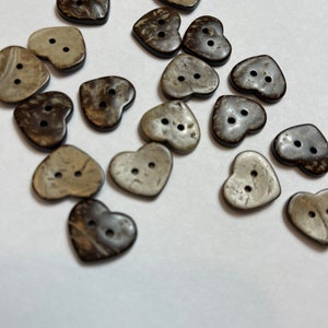 Könnte beinhalten: Eine Sammlung von herzförmigen Kokosnuss-Knöpfen in Braun und Beige. Die Knöpfe haben jeweils zwei Löcher.