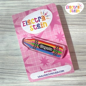 Może przedstawiać: Akrylowa przypinka w kształcie tęczowej kredki z napisem "Gayola" na różowej karcie. Karta zawiera tekst "Electra Stein" i "Acrylic Pin www.electrastein.com" oraz wzór gwiazdy. Kolorowy dodatek.