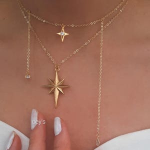 Pode incluir: Colares dourados em camadas com pingentes de estrela e cristal. Os colares apresentam correntes delicadas e um pingente de estrela. A imagem também mostra um anel de ouro e o texto "cey's".
