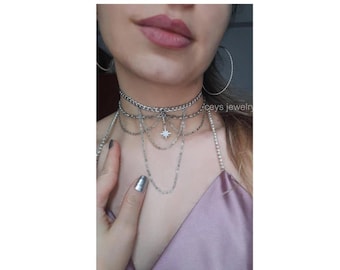 May include: A silver layered choker necklace with a star pendant. The necklace is made of multiple chains of different thicknesses and styles.