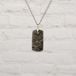 May include: A rectangular pendant featuring a swirling pattern of brown, black, and metallic gold tones, suspended from a silver-toned metal chain. The pendant has a smooth, polished surface with a distinct marbled appearance and a rounded bottom edge.