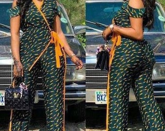May include: Two women wearing a green and yellow patterned jumpsuit with a cold shoulder design. The jumpsuit has a wrap style bodice and a wide leg.