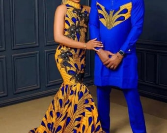 Op de afbeelding: Een stel dat bijpassende traditionele Afrikaanse kleding draagt. De vrouw draagt een gele en blauwe geprinte jurk met een bijpassende hoofddoek. De man draagt een blauw lang mouwen shirt met een geel en blauw geprint ontwerp en een bijpassende broek.