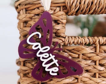 May include: A purple butterfly-shaped tag with the name "Colette" written in white lettering. The tag is hanging from a wicker basket.