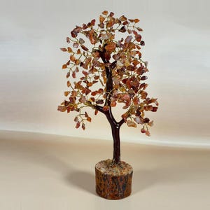 May include: A decorative tree sculpture with a dark brown trunk and branches, adorned with reddish-brown gemstone leaves. The tree sits in a textured, cylindrical base. The leaves are made of small, irregularly shaped stones.