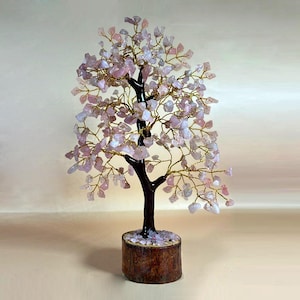 Può includere: Una scultura decorativa a forma di albero con tronco e rami marrone scuro, adornata con foglie di pietre preziose rosa chiaro. L'albero poggia su una base di legno, creando un'estetica naturale ed elegante. I rami sono in filo dorato.
