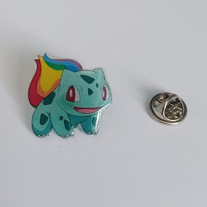 May include: A green and blue cartoon character with a rainbow tail, a pin back, and a silver pin.
