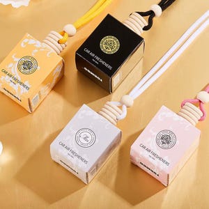 May include: An assortment of car air fresheners in various colors, including yellow, black, white, and pink. Each box-shaped freshener has a wooden top and a string for hanging. The text "CAR AIR FRESHENERS" is printed on the boxes.