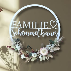 Könnte beinhalten: Ein weißer runder Kranz mit dem deutschen Wort "FAMILIE" und dem Namen "Schimmelbauer" ausgeschnitten. Der Kranz ist mit Trockenblumen in Weiß-, Beige- und Burgundertönen verziert.