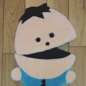 May include: A plush toy of a cartoon character with black hair, a blue shirt, and a large open mouth. The toy is made of soft, fuzzy fabric and has a light brown skin tone.