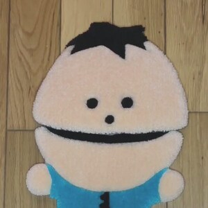May include: A plush toy of a cartoon character with black hair, a white face, and a blue shirt. The toy is made of soft, fuzzy fabric and has a friendly expression.