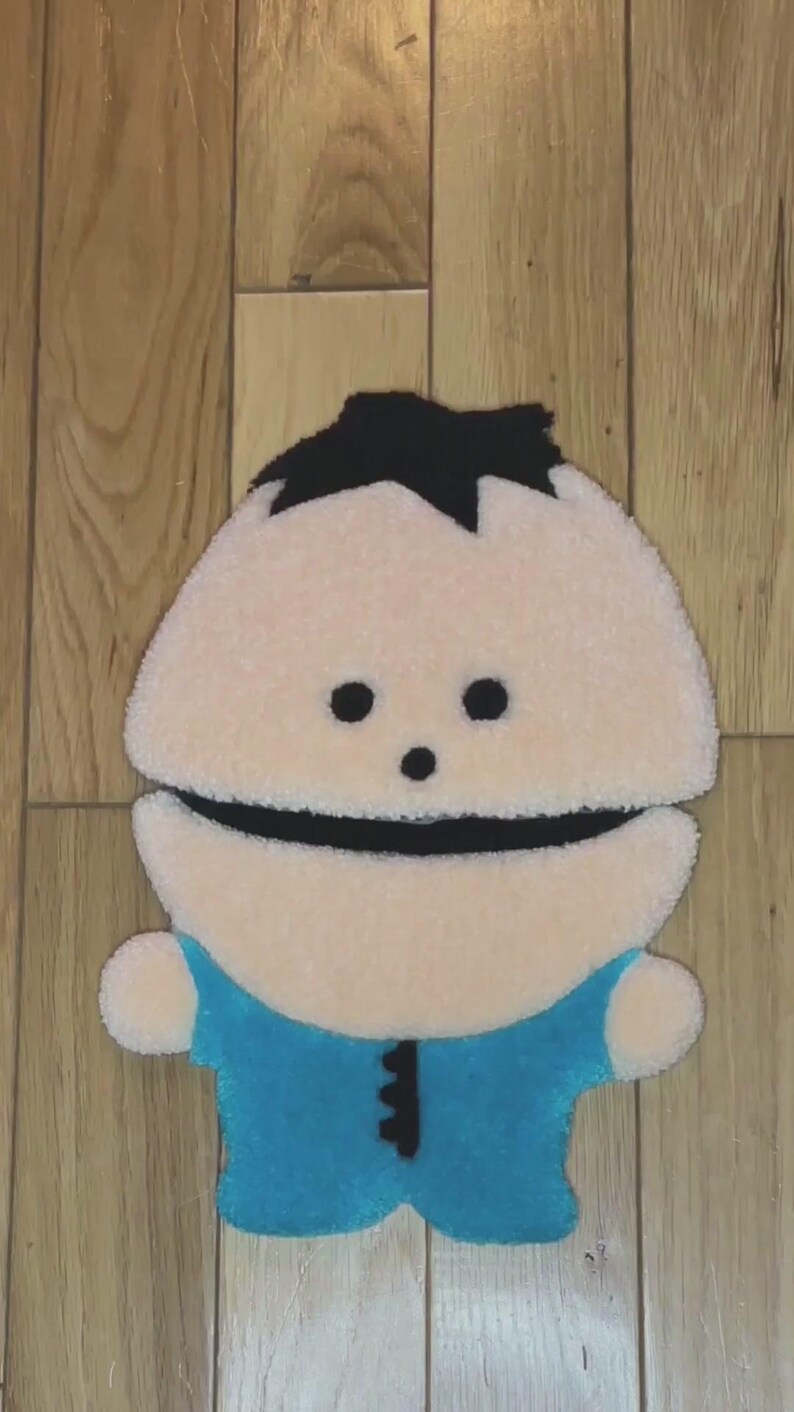 May include: A plush toy of a cartoon character with black hair, a white face, and a blue shirt. The toy is made of soft, fuzzy fabric and has a friendly expression.