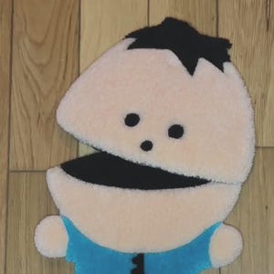 May include: A plush toy of a cartoon character with a black hair, black eyes, a black mouth, and a blue shirt. The toy is made of soft, fuzzy fabric.