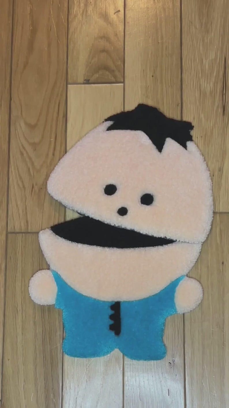 May include: A plush toy of a cartoon character with a black hair, black eyes, a black mouth, and a blue shirt. The toy is made of soft, fuzzy fabric.