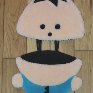 May include: A plush toy of a cartoon character with black hair, a blue shirt, and a pink body. The toy is made of soft, fuzzy fabric.