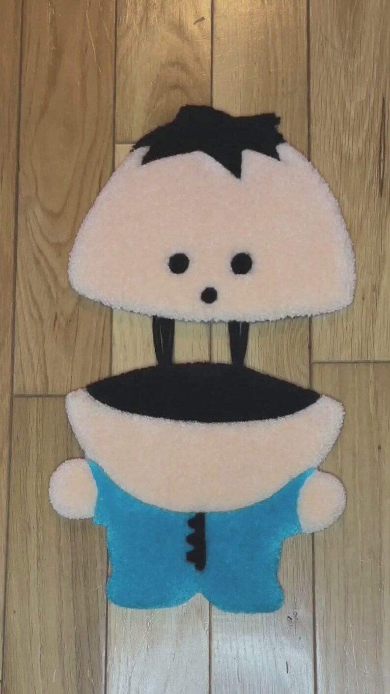 May include: A plush toy of a cartoon character with black hair, a blue shirt, and a pink body. The toy is made of soft, fuzzy fabric.