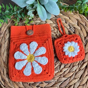 May include: Two crocheted bags with a daisy design. The larger bag is orange with a white daisy and a brown button closure. The smaller bag is orange with a white daisy and a drawstring closure.