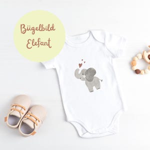 Könnte beinhalten: Weißer Baby Strampler mit einer grauen Elefanten-Illustration und roten Herzen. Der Text "Bügelbild Elefant" befindet sich auf einem gelben Kreis.