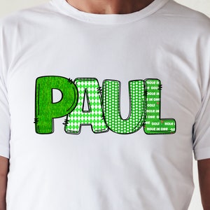 Puede incluir: Camiseta blanca con el nombre "PAUL" escrito en letras verdes con diferentes patrones. Las letras est&aacute;n delineadas en negro. El texto "HOLE is HOLE IN 2 IN ONI GOLF HOLE IN ONE 40 HE GOLF HOLE HOLE IN ONE 40" est&aacute; escrito verticalmente en el lado derecho de la camiseta.