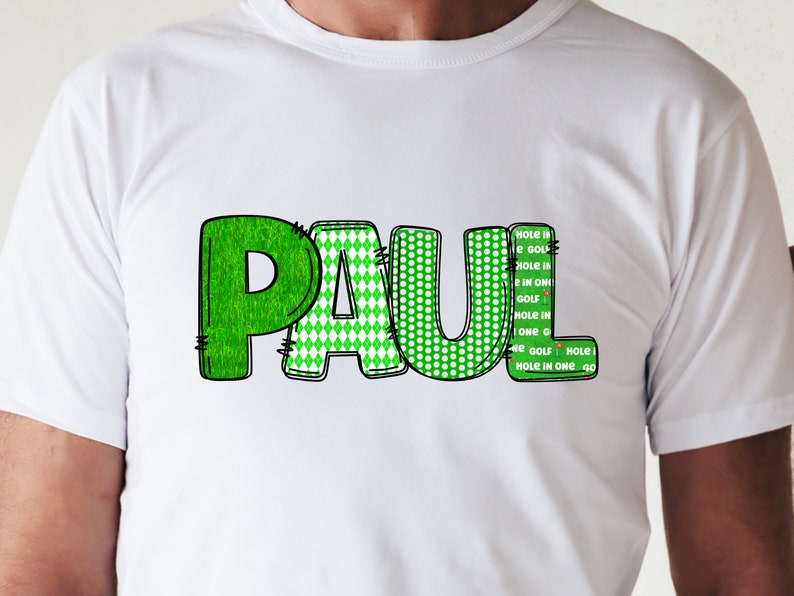 Puede incluir: Camiseta blanca con el nombre "PAUL" escrito en letras verdes con diferentes patrones. Las letras est&aacute;n delineadas en negro. El texto "HOLE is HOLE IN 2 IN ONI GOLF HOLE IN ONE 40 HE GOLF HOLE HOLE IN ONE 40" est&aacute; escrito verticalmente en el lado derecho de la camiseta.