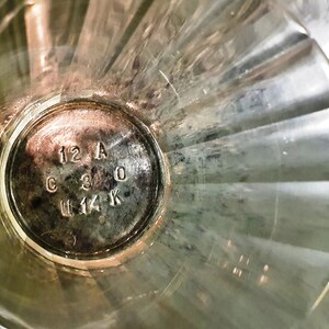 May include: Close-up of the bottom of a clear glass with a silver label that reads "12 A C 3 0 U 14 K".