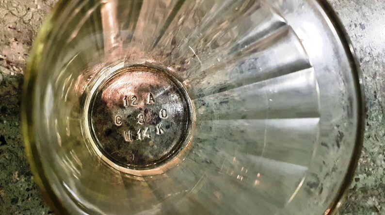 May include: Close-up of the bottom of a clear glass with a silver label that reads "12 A C 3 0 U 14 K".