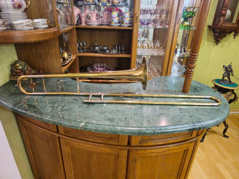 May include: A gold-colored trombone with a bell-shaped mouthpiece. The trombone is lying on a green marble countertop.
