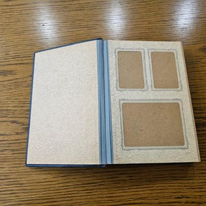 May include: A blue photo album with a white patterned cover and three rectangular photo slots on the inside cover.