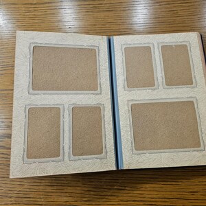 May include: A white photo album with a blue spine and five empty photo slots. The album has a decorative border around each photo slot.