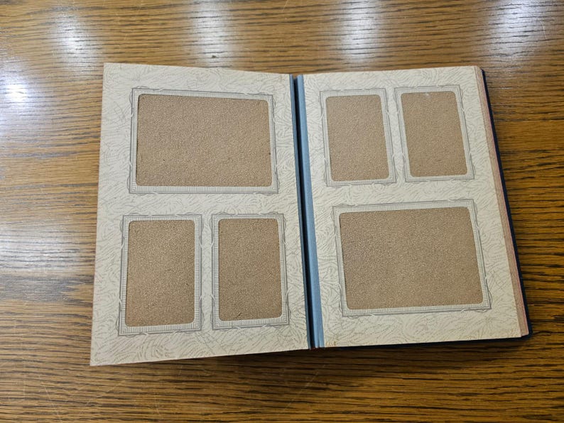 May include: A white photo album with a blue spine and five empty photo slots. The album has a decorative border around each photo slot.