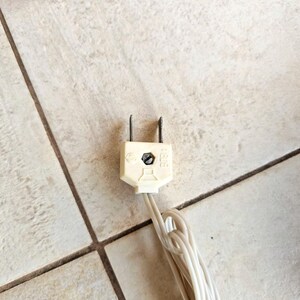 May include: A white electrical plug with two prongs and a white wire attached. The plug has the letters "CE" and "125V" printed on it.