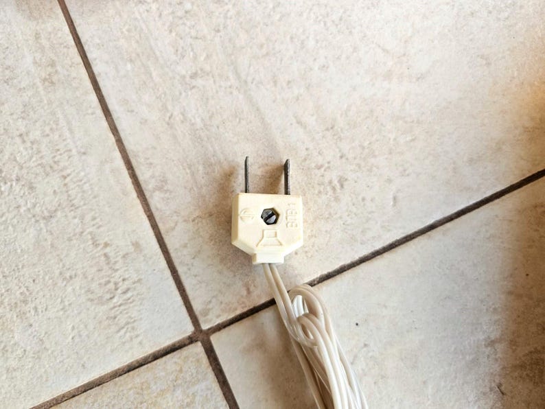 May include: A white electrical plug with two prongs and a white wire attached. The plug has the letters "CE" and "125V" printed on it.