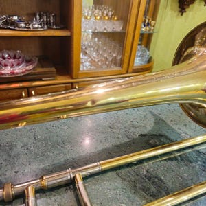 May include: A gold-colored trombone with a shiny finish. The trombone is lying on a green marble surface.