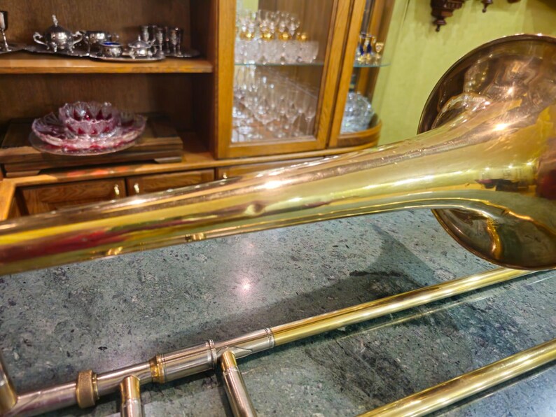 May include: A gold-colored trombone with a shiny finish. The trombone is lying on a green marble surface.