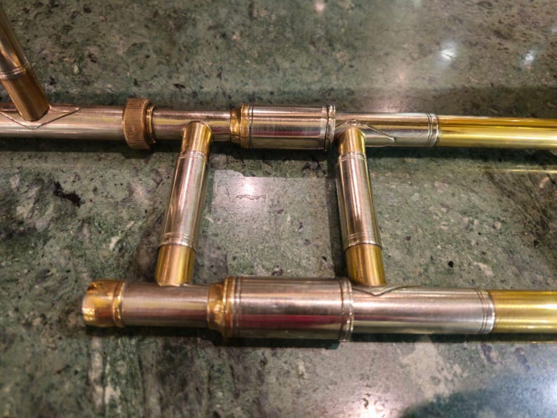 May include: Close-up of the inner workings of a trombone, showing the gold-plated brass tubing and the silver-plated brass slides.